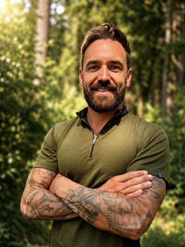 Michael Schneider, Inhaber von Baumschneider, steht lächelnd mit verschränkten Armen im Wald